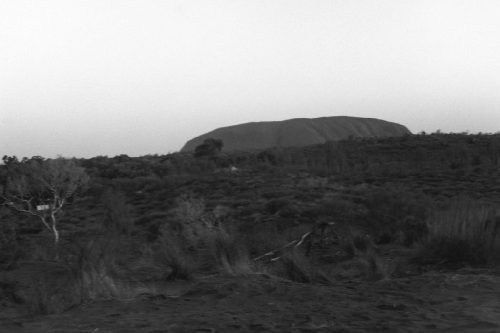 black and white photo of Uluru taken at sunset. The image is tilter slightly.