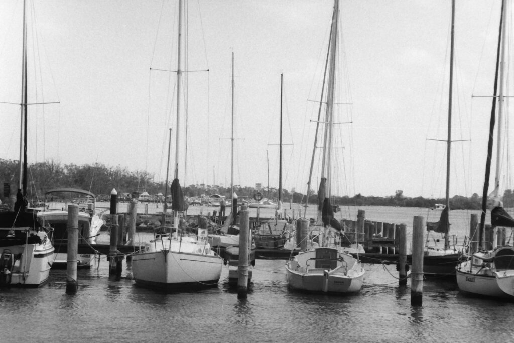 black and white photograph of boats moared at a jetty, with masts standing upright