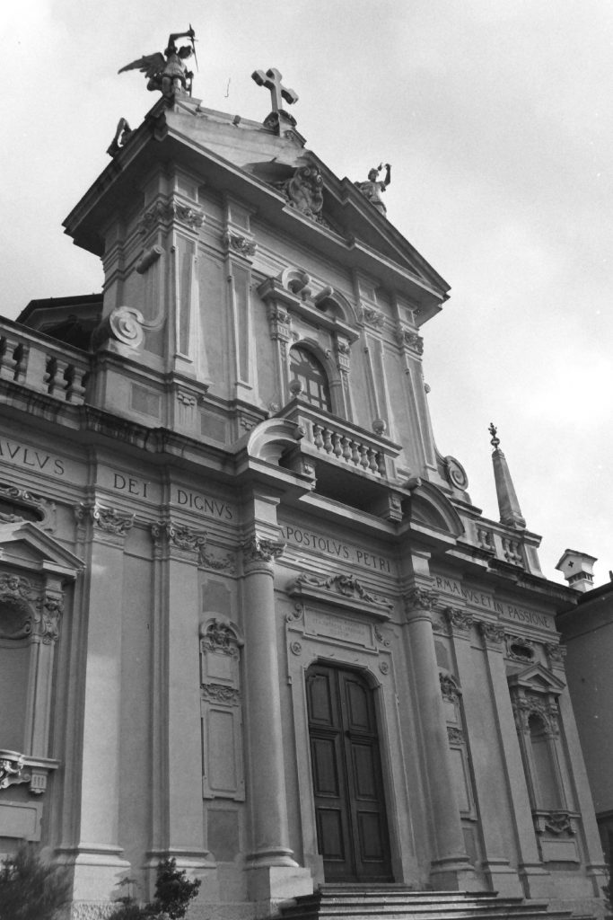 Black and white photograph of a formal stone building with a cross at the top and armed angels either side