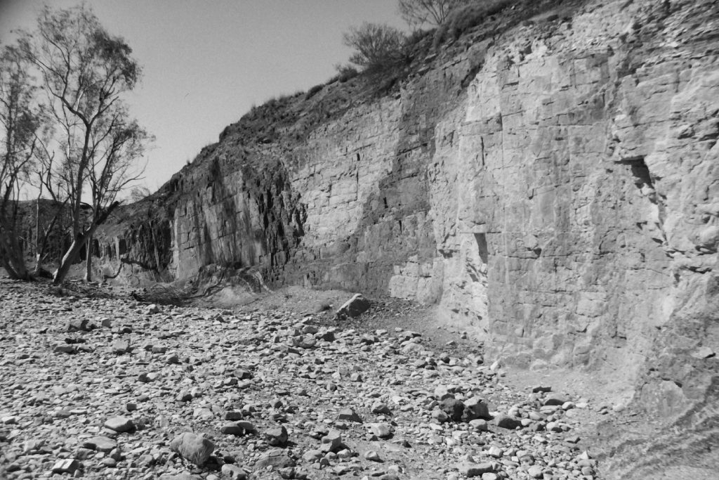 Black and white photograph of a wall of orchre in different shades, carved out by indigenous peoples