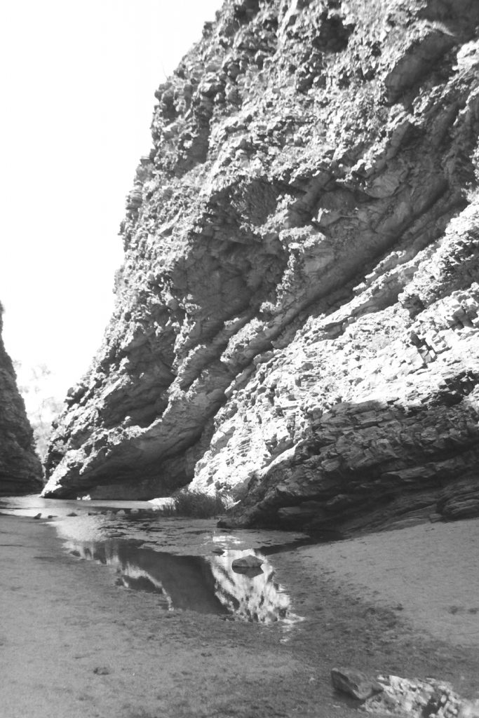 Black and white photograph of a large rock face with a small water pool beneath it