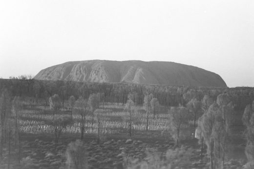 Black and white photo of Uluru at sunrise with the field of lights in the foreground