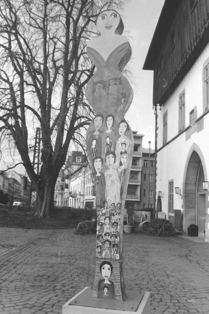 Black and white photograph of a sculpture of a woman with faces of women painted on it