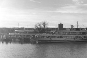 Black and white photograph of car and passenger ferry moored on a lake