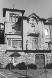 Black and white photograph of a stone house with two front doors, one metal one wooden, with three stories of windows and balconies above