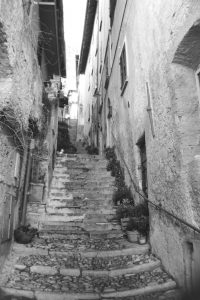 Black and white photograph of stone steps leading up between houses, with doors and windows to the side