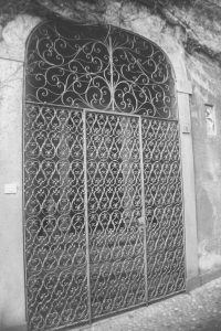 Black and white photograph of a wrought iron gate set into a concrete wall