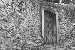 "Black and white photograph of a wooden door set into a stone wall