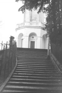 Black and white photograph of stone stairs leading to a white octagonal building, above the a sign reads "A Volta"