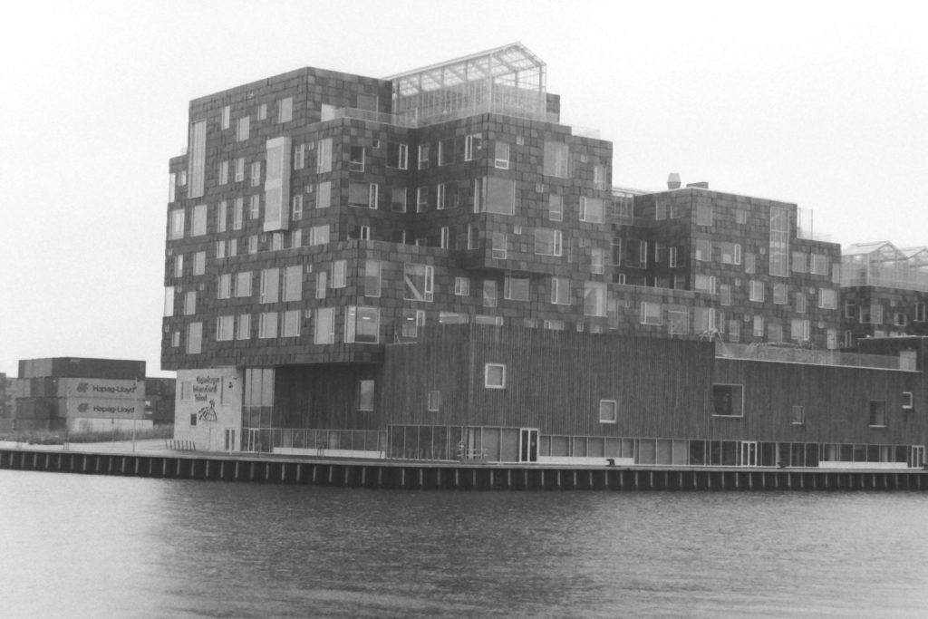 Black and white photograph of a modern building on the harbour. the photo is taken from across the water.