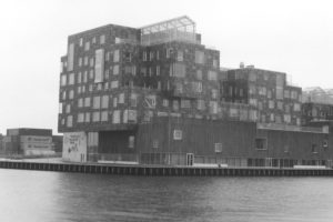 Black and white photograph of a modern building on the harbour. the photo is taken from across the water.