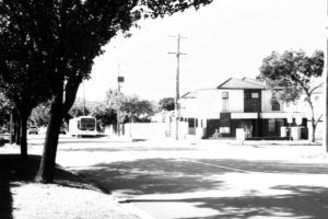 Black and white photograph of a suburban street with a bus approaching