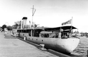 Black and white photo of a navy vessel alongside a pier