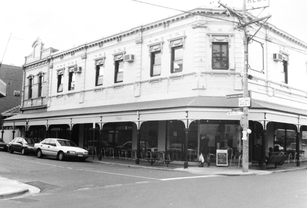 Black and white photo of a street corner with a cafe and parked cars