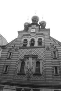 Black and white photo looking up the stone facade of a church, with three onion domes at the top.