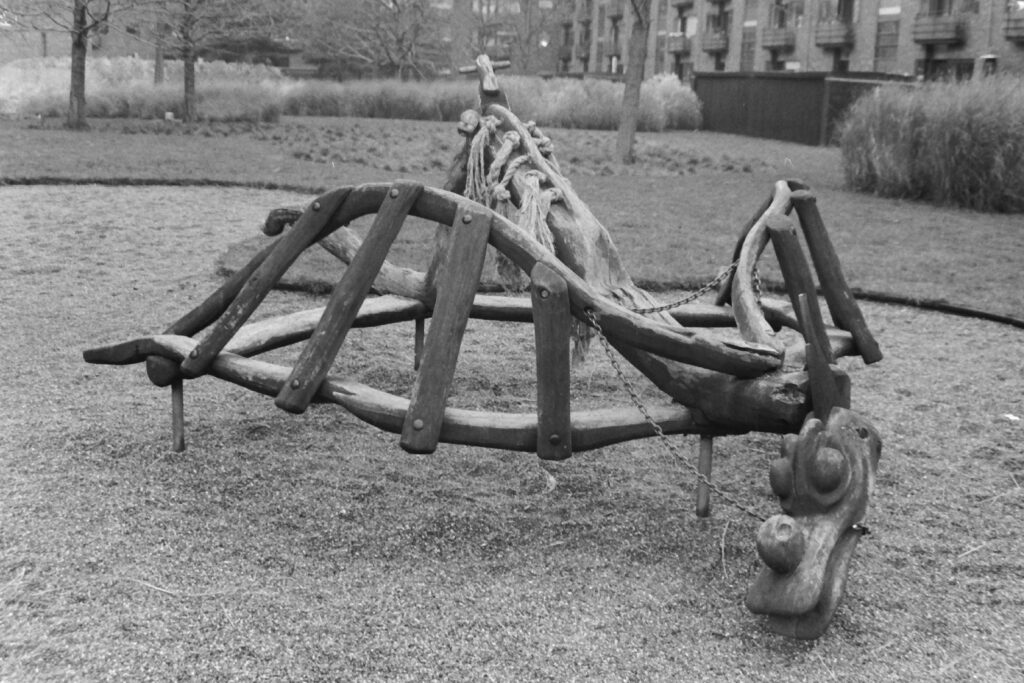 Black and white photo of a wooden playground climbing structure in the shape of a dragon.