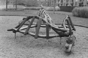 Black and white photo of a wooden playground climbing structure in the shape of a dragon.