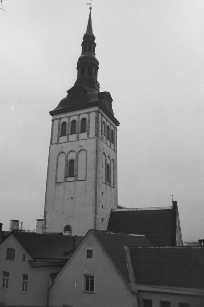 Black and white photo of a church tower surrounded by houses in the foreground.