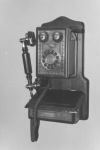 Black and white photo of an antique wooden wall phone. There is a label on it that reads "Reception dial 100".