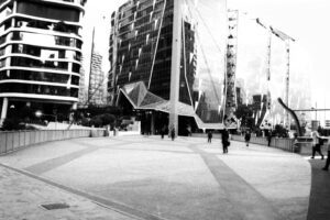 Black and white photo looking towards city buildings, with an almost empty walkway in front