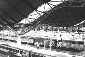 Black and white photo looking out across a city train station, with multiple tracks and a wavy platform roof