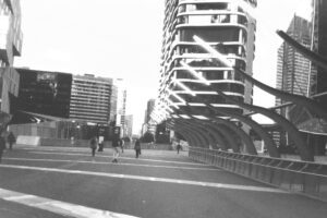 Black and white photo looking towards city buildings, with an almost empty walkway in front and wavy sculptures on the right hand side