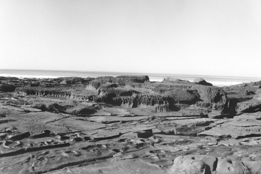 Black and white photo of a rocky outcrop looking over the ocean and waves coming in.