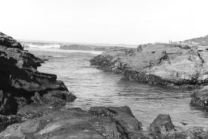 Black and white photos of waves rolling into a rocky channel on a beach.