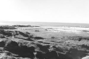 Black and white photo of waves rolling into a rocky alcove on the beach.