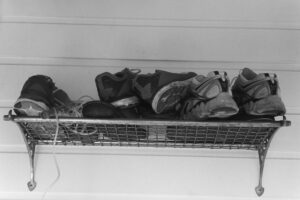 Back and white photo of an old style luggage rack with many pairs of shoes on it and and a skipping rope dangling down.