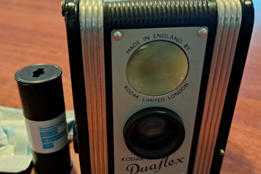 Photo of a Kodak Duaflex camera with a roll of 120 film beside it.