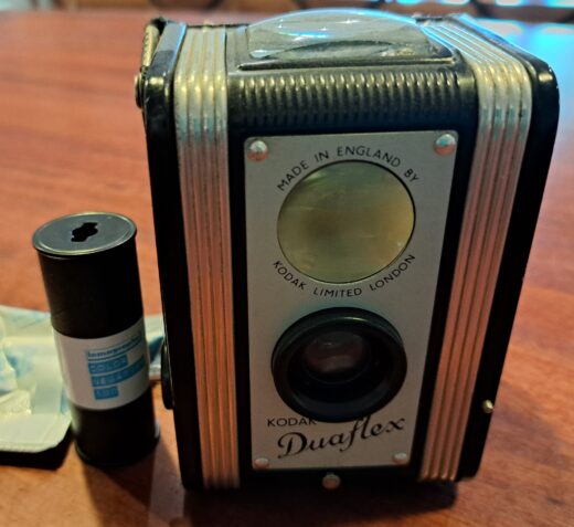 Photo of a Kodak Duaflex camera with a roll of 120 film beside it.