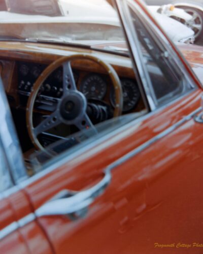 Coffee, Cars and Bikes A close up photograph taken looking into the open window of a red car. The front dashboard and steering wheel are made of polished wood.
