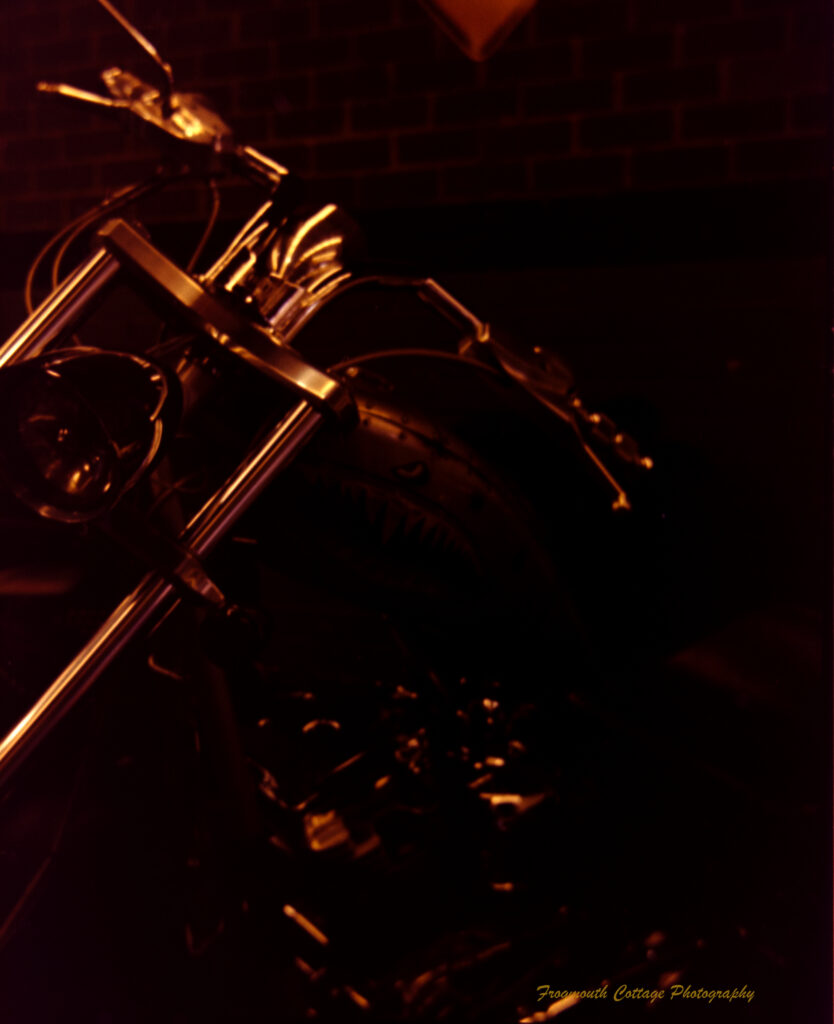 Photograph of the front of a motorcycle frame. The low light is illuminating the steel frame against a dark background.