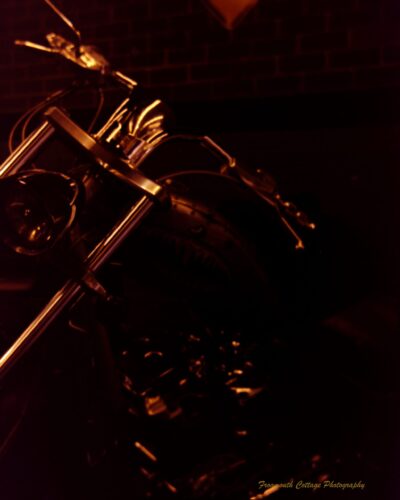 Coffe, Cars and Bikes Photograph of the front of a motorcycle frame. The low light is illuminating the steel frame against a dark background.