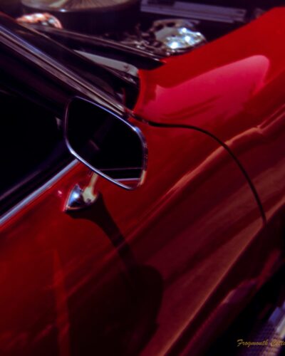 Coffe, Cars and Bikes Close up photo of the side door and mirror of ared car. The shining metal of the engine is just visible as the bonnet is up