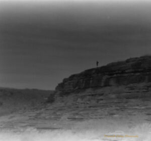 Black and white photo of a large rocky peak with a person standing on top. The photo is a bit blurry.