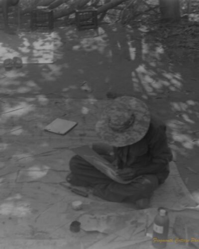 Kakadu National Park Photo of an indigenous artist sitting cross legged on a canvas. He is paining with a thin piece of reed and looking down at his work.