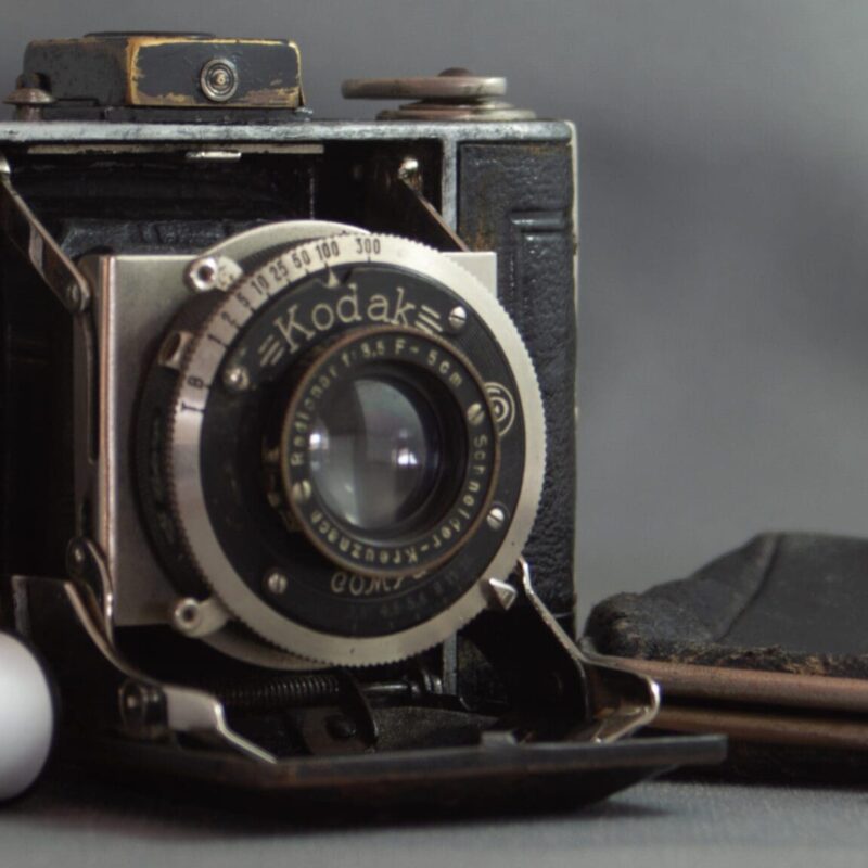 Kodak Vollenda 48 Photograph of a Kodak Vollenda 48 camera - a folding 127 roll film camera. The camera is open with the bellows folded out. There are two rolls of 127 film on the left hand side and a small purse (that the camera fits into) on the other side.