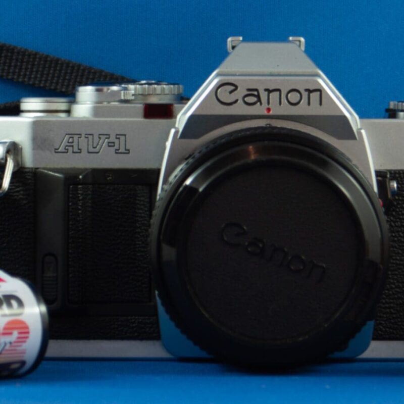 Canon AV-1 Photograph of a Canon AV-1 SLR camera with a strap and three rolls of film.