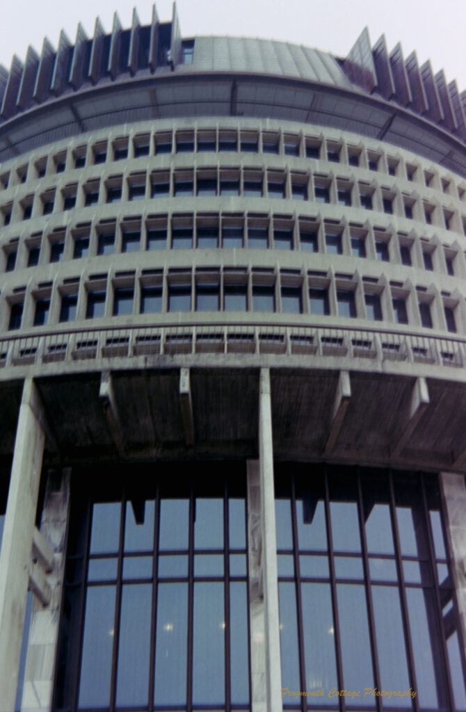 Photo of the front of a circular grey building with tall glass windows at the bottom and smaller square windows above it.