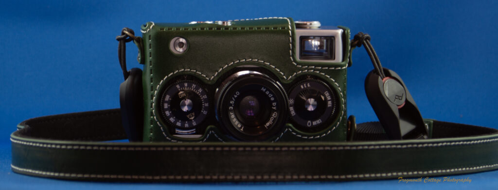 Photograph of a Rollei 35 camera in a green leather case with a matching neck strap lying around it.