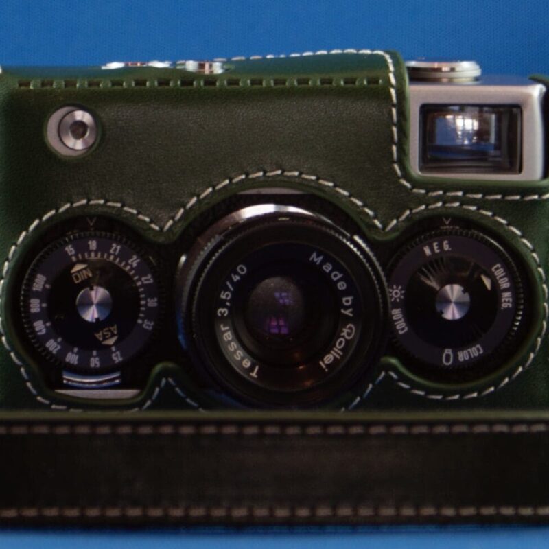 Rollei 35 Photograph of a Rollei 35 camera in a green leather case with a matching neck strap lying around it.