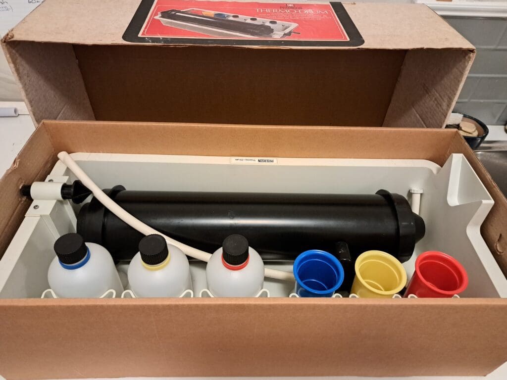 Photograph of a paper developing tank in a box labelled Patterson Therm-Drum