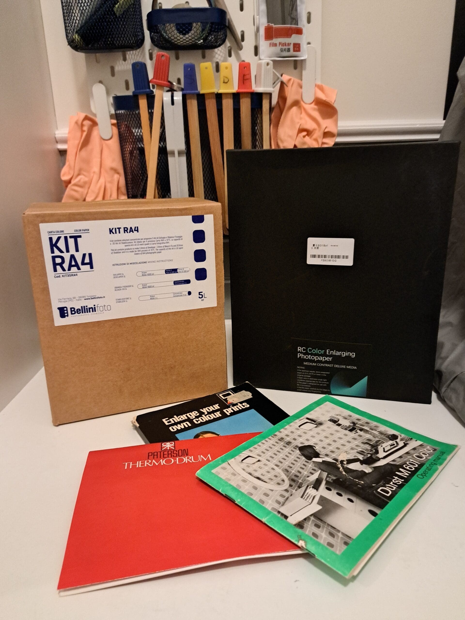 Photograph of a box of RA4 processing chemicals next to a box of colour darkroom paper. In front of the boxes are three booklets relating to colour darkroom printing.