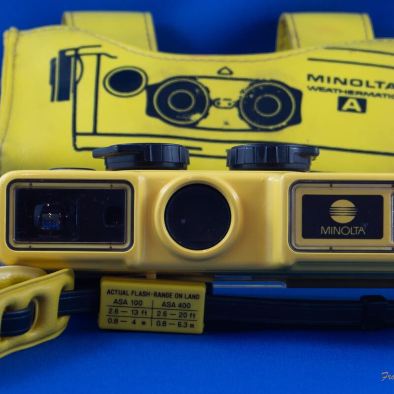 Minolta Weathermatic A Photograph of the Minolta Weathermatic A withwrist strap and the wrap-around case behind it.