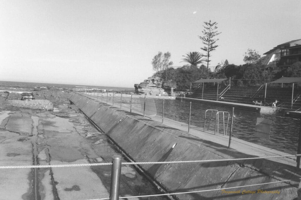 Black and white photograph of a swimming pool built into the rocks beside the ocean.