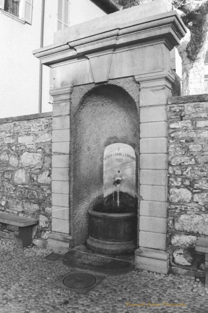 Black and white photo of a stone water alcove with a water tap and basin set inside it.